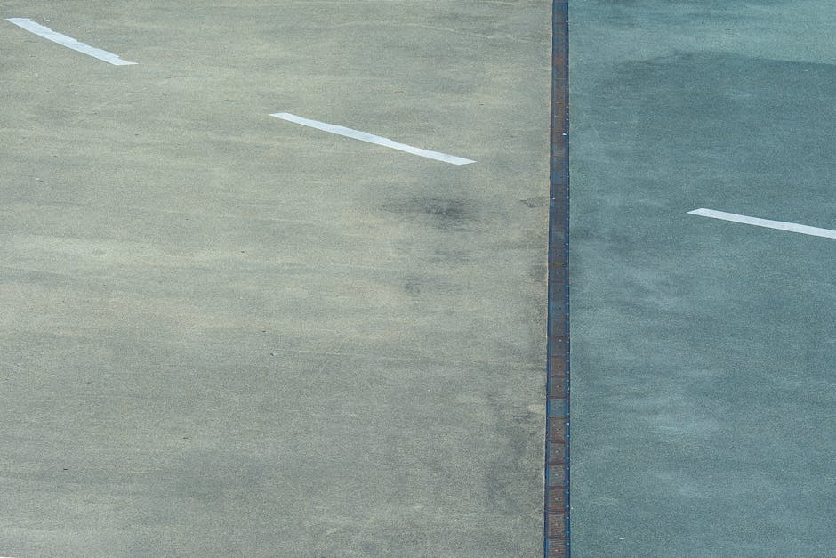 A split view of two parking lot sections shows contrasting surfaces: the left side has a light grey, slightly weathered concrete with faint white painted lines, while the right side features a darker 