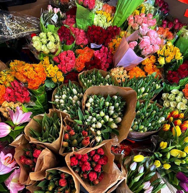 A vibrant display of freshly cut flowers arranged in bouquets at a florist shop, featuring a variety of blooms such as tulips, roses, and lilies in colors including white, pink, red, yellow, orange, a